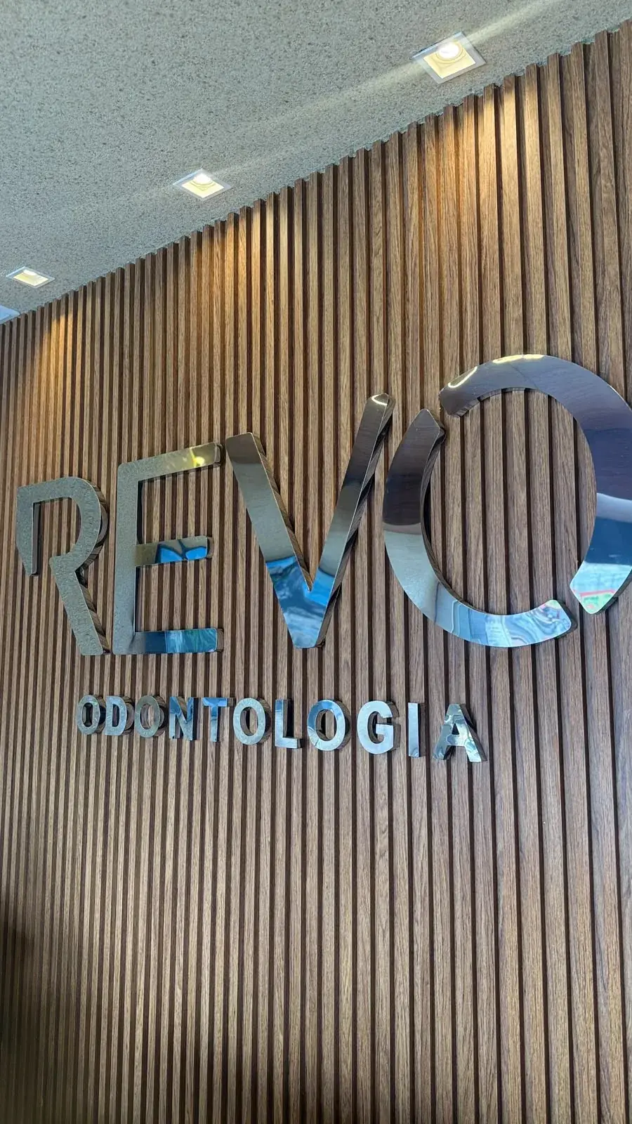 Letreiro da Revo Odontologia no ripado de madeira da recepção